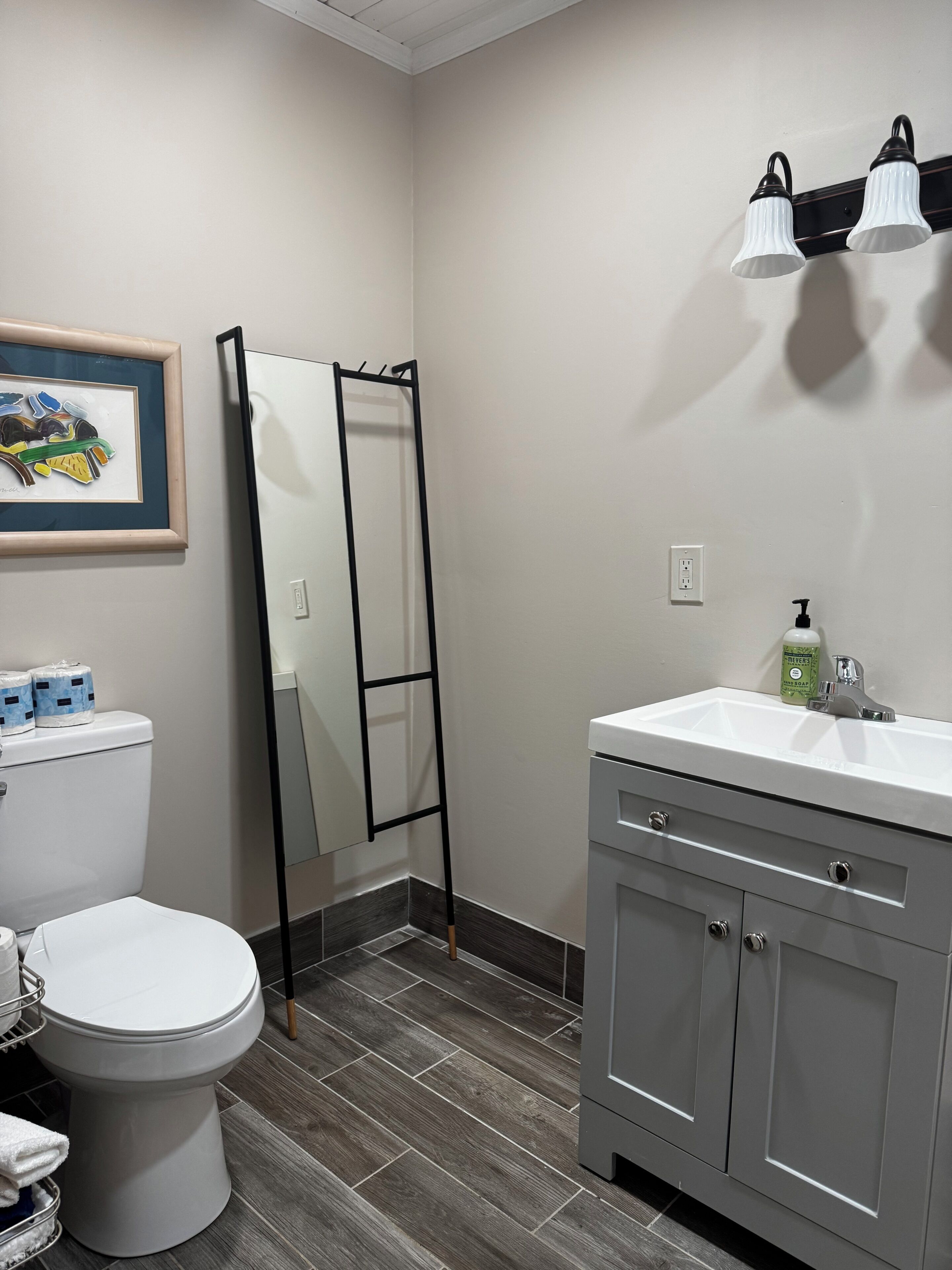 Une salle de bain comprenant des toilettes, un lavabo avec un miroir, une œuvre d’art encadrée et une douche avec une échelle.