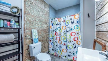 A bathroom with a toilet, a shower curtain with a colorful geometric pattern, and a shelf with toiletries.