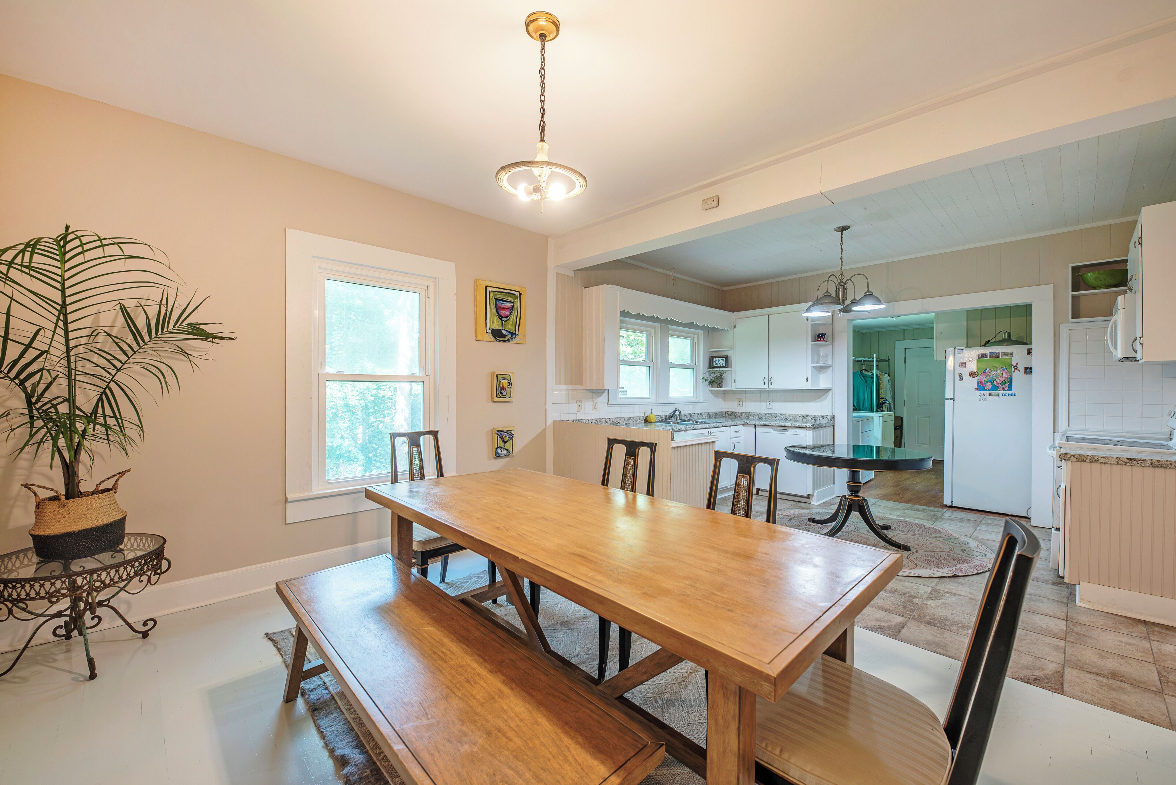 Una cocina amplia con zona de comedor, que incluye una mesa y bancos de madera, una planta en maceta y vistas al comedor contiguo.