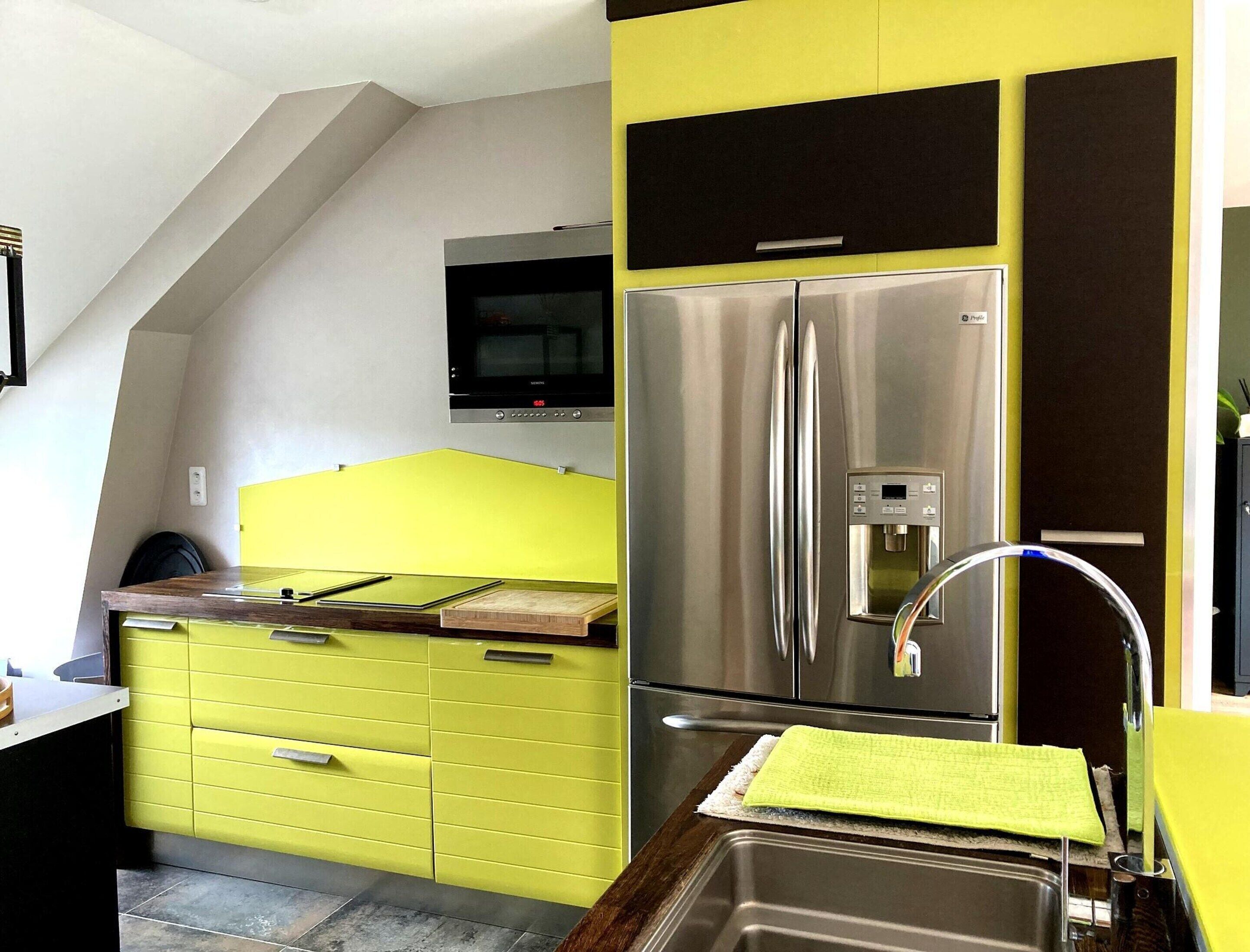 A kitchen with a stainless steel refrigerator, a microwave, and a yellow cabinet.