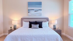 A bedroom with a large bed, two bedside tables with lamps, a painting above the bed, and a window on the right. - Bayou Breeze  - Pool + Waterfront Views + 8 Minutes to Downtown Pensacola (Pensacola)