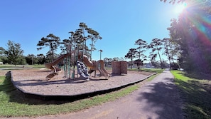 A playground with slides and climbing structures, surrounded by grass and trees. - Bayou Breeze  - Pool + Waterfront Views + 8 Minutes to Downtown Pensacola (Pensacola)