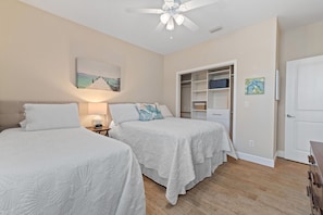 A bedroom with two beds, a ceiling fan, a painting, a closet, and a door. - Bayou Breeze  - Pool + Waterfront Views + 8 Minutes to Downtown Pensacola (Pensacola)