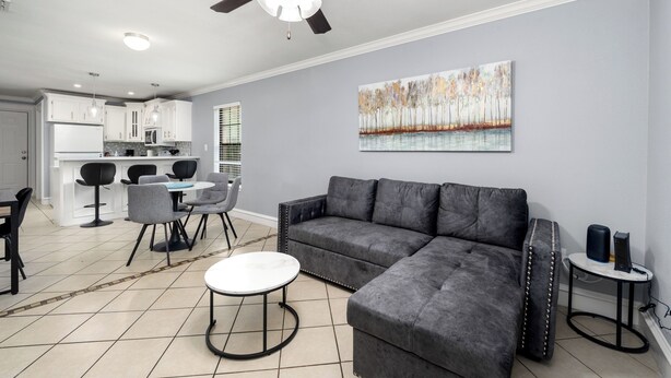 A modern living room with a sectional sofa, a round coffee table, a dining area with chairs, a kitchen with white cabinets, and a ceiling fan. - The C4 Gateway to Starbase (Brownsville)