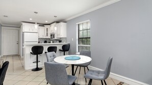 A modern kitchen with white cabinets, a central island, and a dining area with grey chairs and a round table. - The C4 Gateway to Starbase (Brownsville)