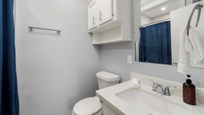 A bathroom with a white toilet, a sink with a mirror, and a shower curtain. - The C4 Gateway to Starbase (Brownsville)