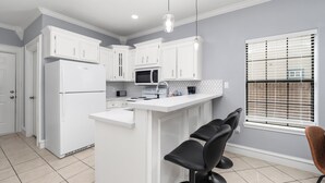 A modern kitchen with white cabinetry, a built-in microwave, and a bar area with two black bar stools. - The C4 Gateway to Starbase (Brownsville)