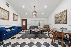 A living room with a blue sofa, a wooden coffee table, a dining table with chairs, and a chandelier. - Bright and Peaceful Modern Home - Sleeps 5 (Sanford)