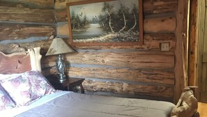 Ein Blockhausszimmer mit Bett, Lampe, einem Waldgemälde und einem Holzkopfteil.
