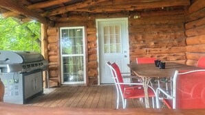 Eine Holzhütte mit Grill, Tür und Tisch mit roten Stühlen.
