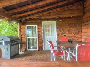 A wooden cabin with a grill, a door, and a table with red chairs.