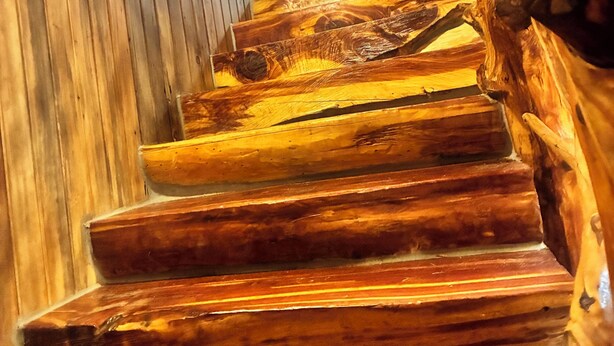Eine Holztreppe mit Handlauf, die zu einem Raum mit einer Holzwand und einem gerahmten Bild führt.