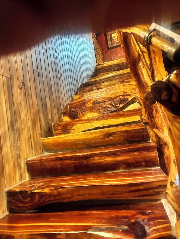 A wooden staircase with a handrail, leading to a room with a wooden wall and a framed picture.
