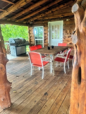 Una terraza de madera con mesa y sillas, una parrilla y una puerta con ventanas.