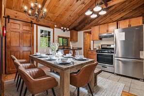 A wooden-paneled kitchen with a dining table set for four, a stainless steel refrigerator, and a built-in oven. - Cozy 3-bedroom cabin in Blue Ridge with stargazing deck and hot tub (Blue Ridge)