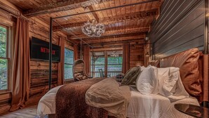 Ein Schlafzimmer in einer Holzhütte mit einem Bett, einem Fernseher, einem Hängesessel und Blick ins Freie.