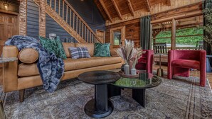 Ein gemütliches Blockhaus-Interieur mit einer Holztreppe, einem Ledersofa, einem Glastisch und einem roten Sessel.