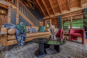 Ein gemütliches Blockhaus-Interieur mit einer Holztreppe, einem Ledersofa, einem Glastisch und einem roten Sessel.
