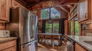 Eine rustikale Küche mit Holzausbau, einem Edelstahlkühlschrank, einer Arbeitsplatte aus Granit und einem Essbereich mit Stühlen.