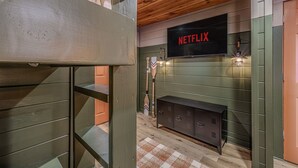 Ein Etagenbett, ein Fernseher mit 'NETFLIX' auf dem Bildschirm, eine Holzbalkendecke und eine grüne Wand mit Kamin.