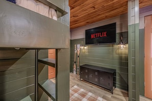 Ein Etagenbett, ein Fernseher mit 'NETFLIX' auf dem Bildschirm, eine Holzbalkendecke und eine grüne Wand mit Kamin.
