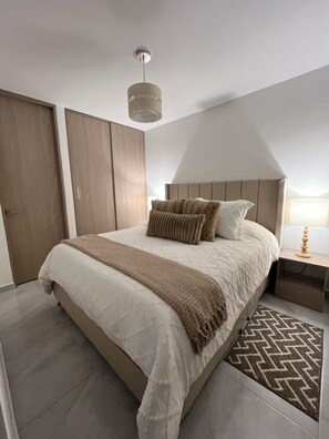 A bedroom with a bed, a bedside table, a lamp, a hanging light fixture, and a wardrobe.
