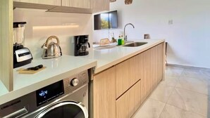 A modern kitchen with wooden cabinets, a built-in washing machine, a coffee maker, and a sink.