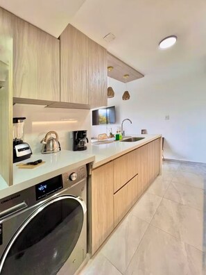 A modern kitchen with wooden cabinets, a built-in washing machine, a coffee maker, and a sink.