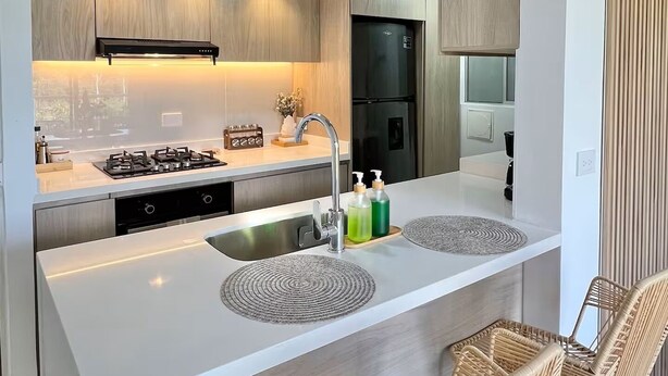 A modern kitchen with a central island, stainless steel appliances, and wicker chairs.