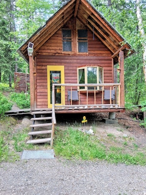 Une cabane en bois avec une véranda, une porte et une fenêtre.