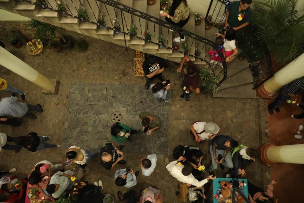 A crowded indoor space with a central area for socializing, a staircase with potted plants, and a stone floor.