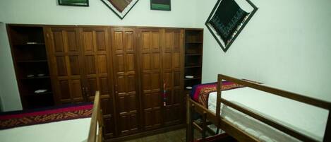 A room with a bunk bed, wooden wardrobe, and wall-mounted shelves.