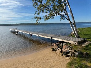 A wooden dock extending into a calm lake, surrounded by a grassy area with rocks. - Secluded Portage Lake Home - Bootjack Shores - New Construction (Lake Linden)