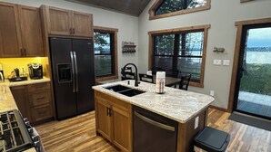 Une cuisine moderne avec des meubles en bois, un réfrigérateur en acier inoxydable, un plan de travail en granit et de grandes fenêtres.