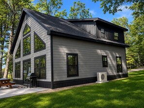 A modern two-story house with large windows, a patio, and an air conditioning unit. - Secluded Portage Lake Home - Bootjack Shores - New Construction (Lake Linden)