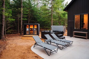 A modern outdoor living area with a hot tub, lounge chairs, and a small cabin-like structure with glass doors. - Cozy Lakefront Retreat | Sauna, Hot Tub & Ski (Wild Rose)