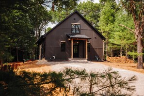 A modern two-story building with a dark exterior, a front porch, and a driveway leading to the entrance. - Cozy Lakefront Retreat | Sauna, Hot Tub & Ski (Wild Rose)