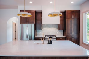 A modern kitchen with a central island, stainless steel appliances, and wooden cabinetry. - Cozy Lakefront Retreat | Sauna, Hot Tub & Ski (Wild Rose)