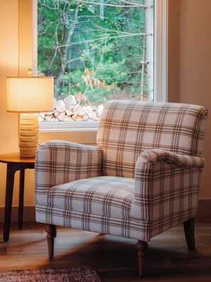 A plaid armchair with wooden legs, positioned next to a lamp and a small table, with a window in the background. - Cozy Lakefront Retreat | Sauna, Hot Tub & Ski (Wild Rose)