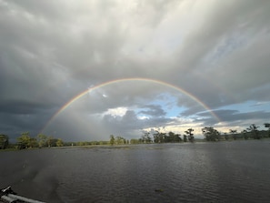 Paisagem com um arco-íris que se estende sobre a água, cercada por árvores.