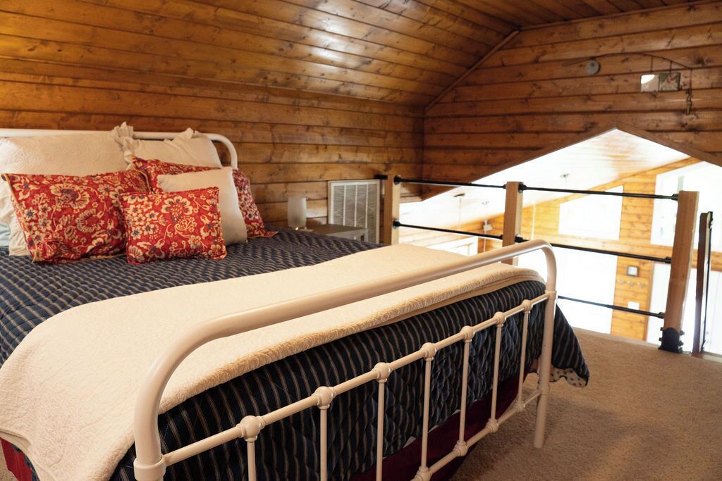 A wooden cabin bedroom with a bed, pillows, and a view of the outside.