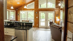 A cabin interior with a kitchen, dining area, and a seating area with a view of the outdoors.