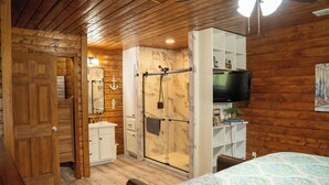 A wooden interior with a bed, a TV, a shower, and a white cabinet.