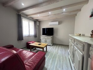 A living room with a red leather sofa, a wooden table, a television on a cabinet, and a kitchen area with cabinets. - The Provençal Address - 1-Bedroom Apartment with Terrace · Indoor Pool · Air Conditioning · Puyricard (Aix-en-Provence)