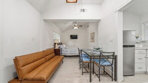 Un espacio habitable compacto con sofá, mesa de comedor, sillas, ventilador de techo y una zona de cocina.
