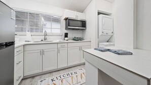 Una cocina moderna con armarios blancos, microondas, hervidor y ventana con persianas.