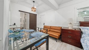 Una habitación con una mesa de comedor de vidrio, un sofá marrón, un aparador de madera y una ventana con persianas.