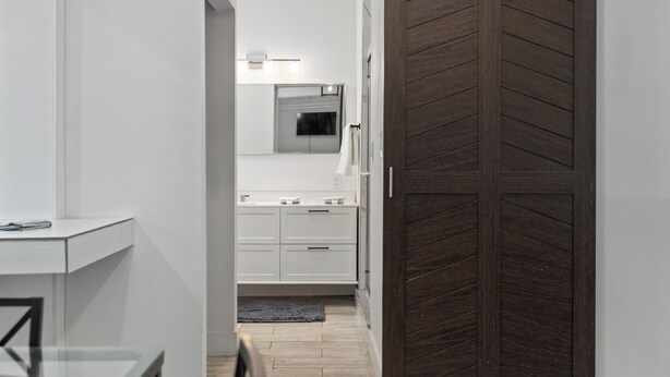 Pasillo que conduce a un baño con espejo, perchero y puerta de madera.