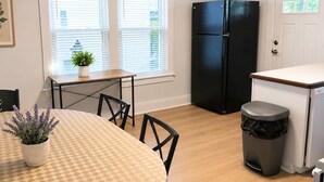 Een kleine keuken met een eettafel, stoelen, een koelkast en een prullenbak.