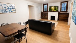 Een woonkamer met een eettafel, zwarte bank, open haard en kunstwerken aan de wanden.